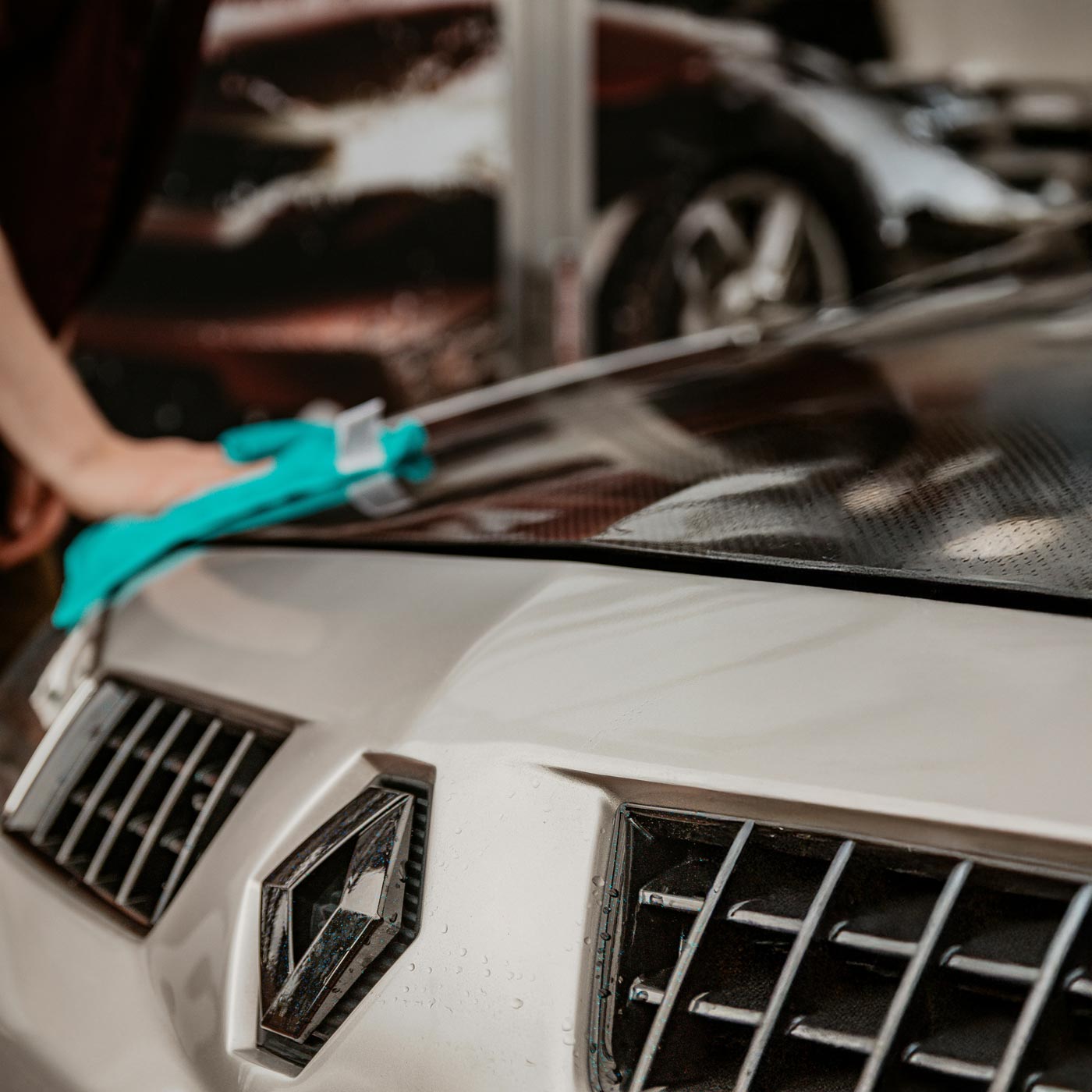 Ruka v ochranné rukavici leští kapotu auta hadříkem.